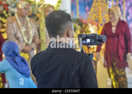 a videographer who documents traditional Javanese weddings using a mirrorless camera and gimbal stabilizer in Tulungagung, Indonesia, 2 July 2023. Stock Photo