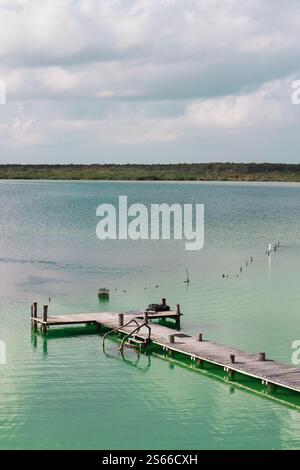 Shot at the Kaan Luum Lagoon in Tulum, Quintana Roo, Mexico, the wooden dock extends into the water on a cloudy summer day. Stock Photo