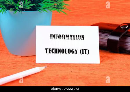 Startup office or people teamwork concept. INFORMATION TECHNOLOGY (IT) written on a white business card on an orange background. Stock Photo