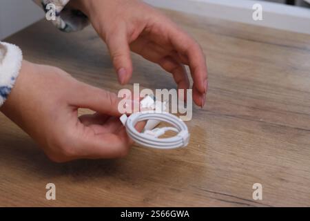 A woman is demonstrating a charger for gadgets. The power adapter and cable are white. Stock Photo