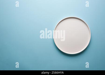 Top view of empty ceramic white plate on blue background Stock Photo