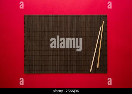 Sushi sticks and empty bamboo mat on red background Stock Photo