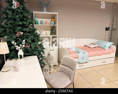Beautiful bedroom interior featuring a decorated Christmas tree, stylish bedding, and minimalist furniture for a cozy and festive atmosphere. Stock Photo