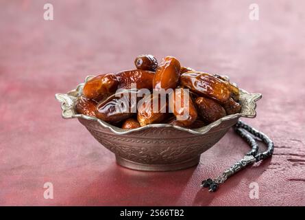 Bowl full of dates and  tasbih (misbaha) on old red-brown wooden table. Stock Photo