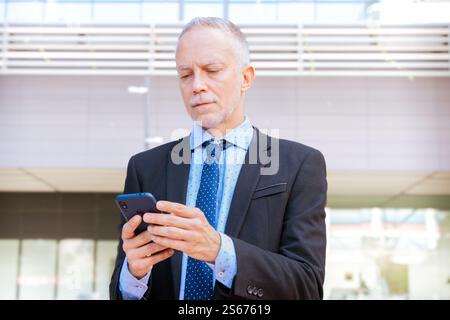 Smiling businessman using an application on his smartphone and standing. Stock Photo