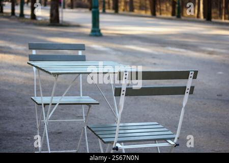 an empty cafe table with two chairs placed on a paved path in a park. Stock Photo