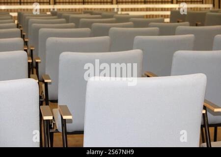 An empty fragment of a conference hall or auditorium with rows of gray chairs with wooden arms. Stock Photo