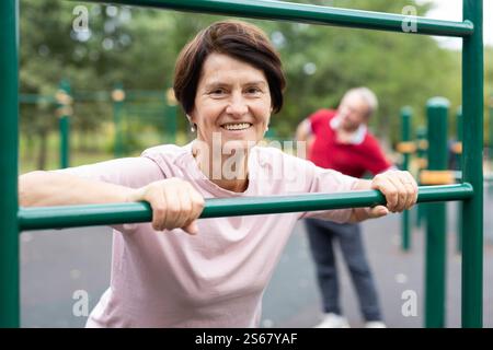 Mature woman doing push-ups from the crossbar on outdoor sports ground Stock Photo