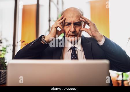 Close up photo of frustrated senior businessman in suit having a headache while working on laptop in city cafe. Stock Photo