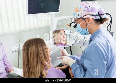 Female dentist pointing at mirror, showing treatment result to satisfied patient in dental clinic Stock Photo
