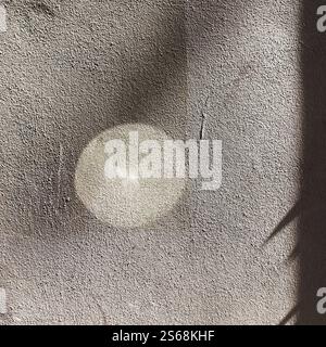 Abstract composition of light reflection creating a circular glow on textured wall, complemented by tender shadows, evoking calmness. Stock Photo