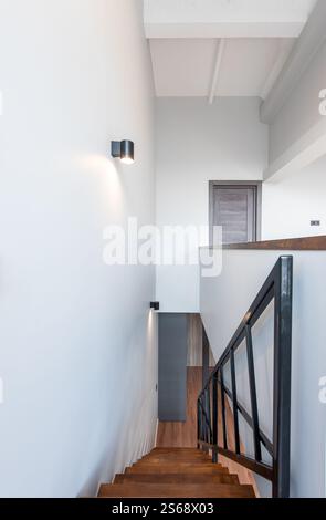 Sleek modern staircase interior featuring wooden steps, metal railings, bright wall lighting, and clean minimalist aesthetics emphasizing contemporary Stock Photo