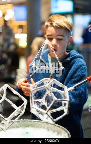 Child exploring science and having fun creating geometric soap bubbles with metal frames at a museum Stock Photo