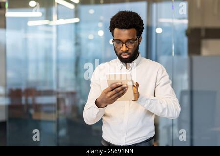 Serious thinking man standing with tablet computer in the middle of the office, businessman working in the evening, using online application to view online financial investment reports. Stock Photo