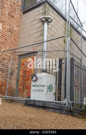 A proactive portable camera security system installed behind security fencing and positioned in front of an unused building to help deter trespassers Stock Photo