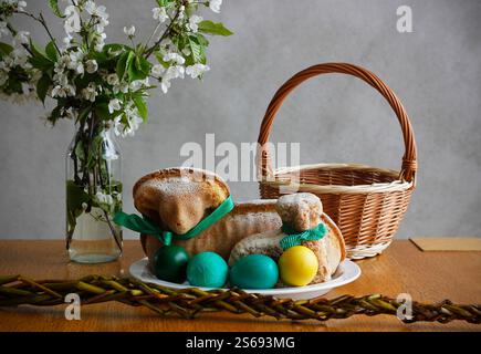 Easter still life containing two lamb cakes, four painted eggs, a wicker basket, an Easter whip and and blooming cherry twigs in a vase Stock Photo