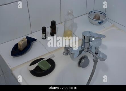 Paris, France - 01 12 2025: Two soaps, two bottles of essential oils, a homemade shower gel and a pumice stone on the edge of a bathtub Stock Photo