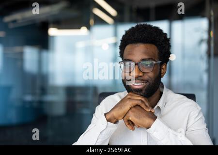 Successful dreamy man looking out the window close up. Businessman satisfied with results of activity reaching out, working inside the office. Stock Photo