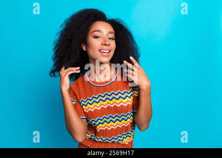 Photo portrait of beautiful young girl wearing brown ornament stylish t shirt touching black curls isolated on blue color background Stock Photo