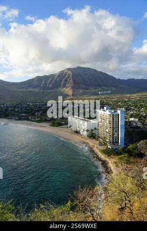 Scenic coastal view on Oahu, Hawaii, featuring a stunning beach, a towering building by the shore, and mountains in the background under a blue sky Stock Photo