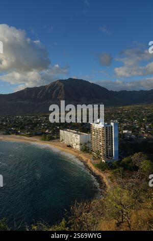 Scenic coastal view on Oahu, Hawaii, featuring a stunning beach, a towering building by the shore, and mountains in the background under a blue sky Stock Photo