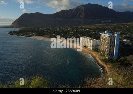 Scenic coastal view on Oahu, Hawaii, featuring a stunning beach, a towering building by the shore, and mountains in the background under a blue sky Stock Photo