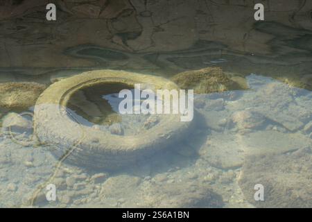 An old tire and additional waste have been discarded into the small water stream that flows through the town, with the tire now overgrown with algae. Stock Photo