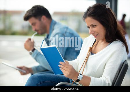 woman reading a book and man looking at tablet outdoors Stock Photo