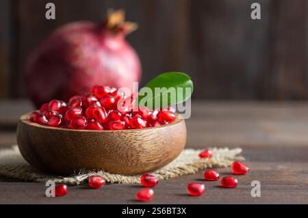 Fresh ripe whole and split juicy pomegranate with seeds and leaves on wooden rustic background, healthy red fruits concept copy space (Punica granatum Stock Photo