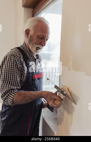 Senior man plastering wall around window because of house renovation Stock Photo