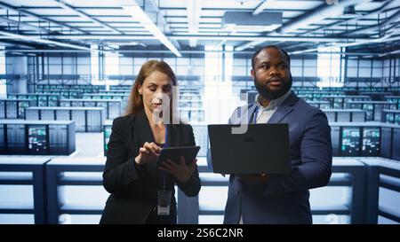 Manager in data center supervising worker running error checking utilities to fix errors. Supervisor in server farm overseeing engineer repairing network issues affecting rigs performance, camera B Stock Photo