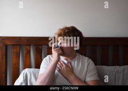 Young man sitting on bed using inhailer for asthma attack Stock Photo