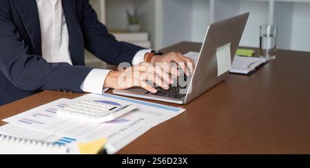 Elderly businessman typing on a laptop while analyzing financial data in an office Stock Photo