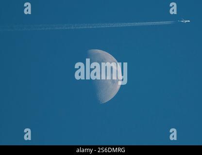 A jet streams contrails as it passes the moon in the afternoon sky over New Jersey. Stock Photo