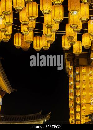 Dali, China - November 19, 2024 : Hundreds of glowing amber lanterns hang against a dark night sky, illuminating a traditional building's architecture Stock Photo