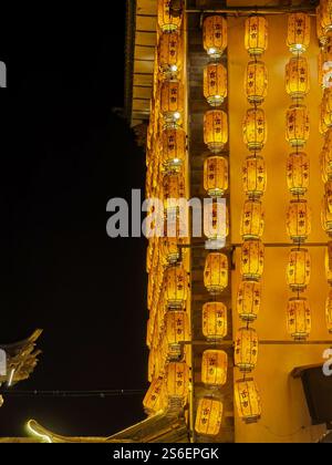 Dali, China - November 19, 2024 : Illuminated building at night, adorned with numerous warm-toned paper lanterns hanging vertically.  The scene evokes Stock Photo
