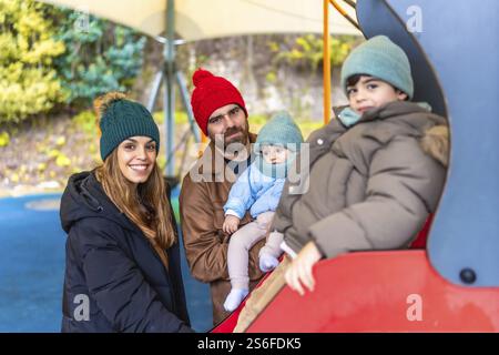 Smiling family enjoying a day at the playground, with children playing on a slide during the fall season Stock Photo