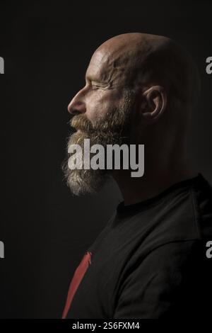 An image of a bearded man with closed eyes side view and dark background Stock Photo
