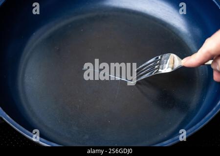 Fork scratching the non stick coating on a frying pan Stock Photo
