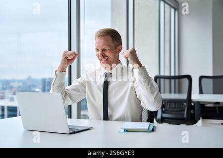 Excited business man winner celebrating success looking at laptop in office. Stock Photo