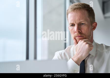 Busy serious young business man looking at laptop thinking working in office. Stock Photo