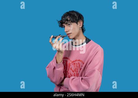 Young man holding smartphone near mouth, using virtual assistant, recording voice message, or talking on speakerphone Stock Photo