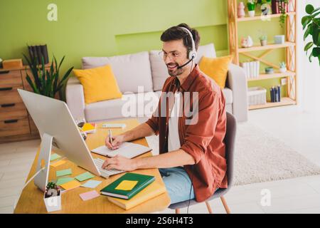 Young man working remotely in a cozy home office space with vibrant decor, wearing headphones Stock Photo