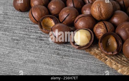Macadamia nuts in cracked shells are arranged neatly on a rustic wooden surface, showcasing their rich brown color and texture. Stock Photo