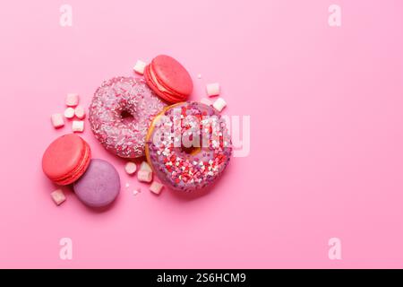 An eye-catching arrangement of colorful macarons and donuts on a pastel pink background. Perfect for showcasing desserts or sweet treats with a playfu Stock Photo