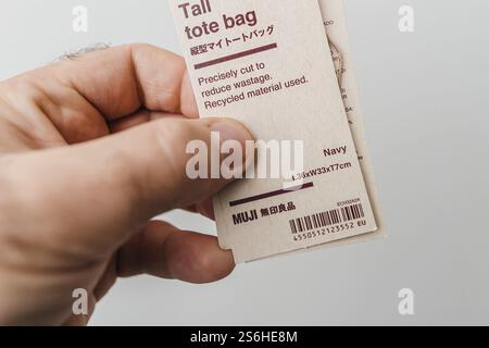 Paris, France - Oct 25, 2023: A close-up of a hand holding a MUJI tall tote bag label, highlighting eco-friendly features, dimensions, and recycled ma Stock Photo