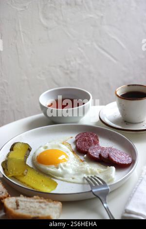 Scrambled eggs, smoked sausage and pickles in a plate on the table. Stock Photo