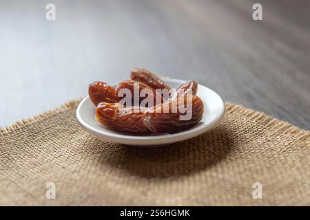 A close-up of a small bowl of dried dates on a rustic burlap background. Stock Photo