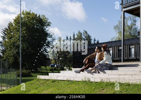 Couple sitting outside on a terrace wooden stair and looking away Stock Photo