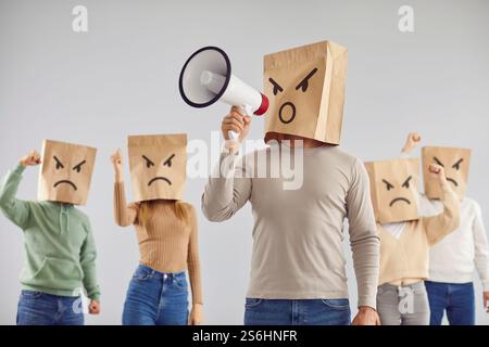 Man in paper bag mask on head shouting in megaphone with angry crowd of protesting people Stock Photo
